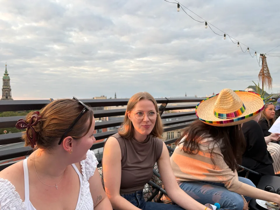 Kolleginnen sitzen im Gespräch am Terrassengeländer, eine mit Sombrero