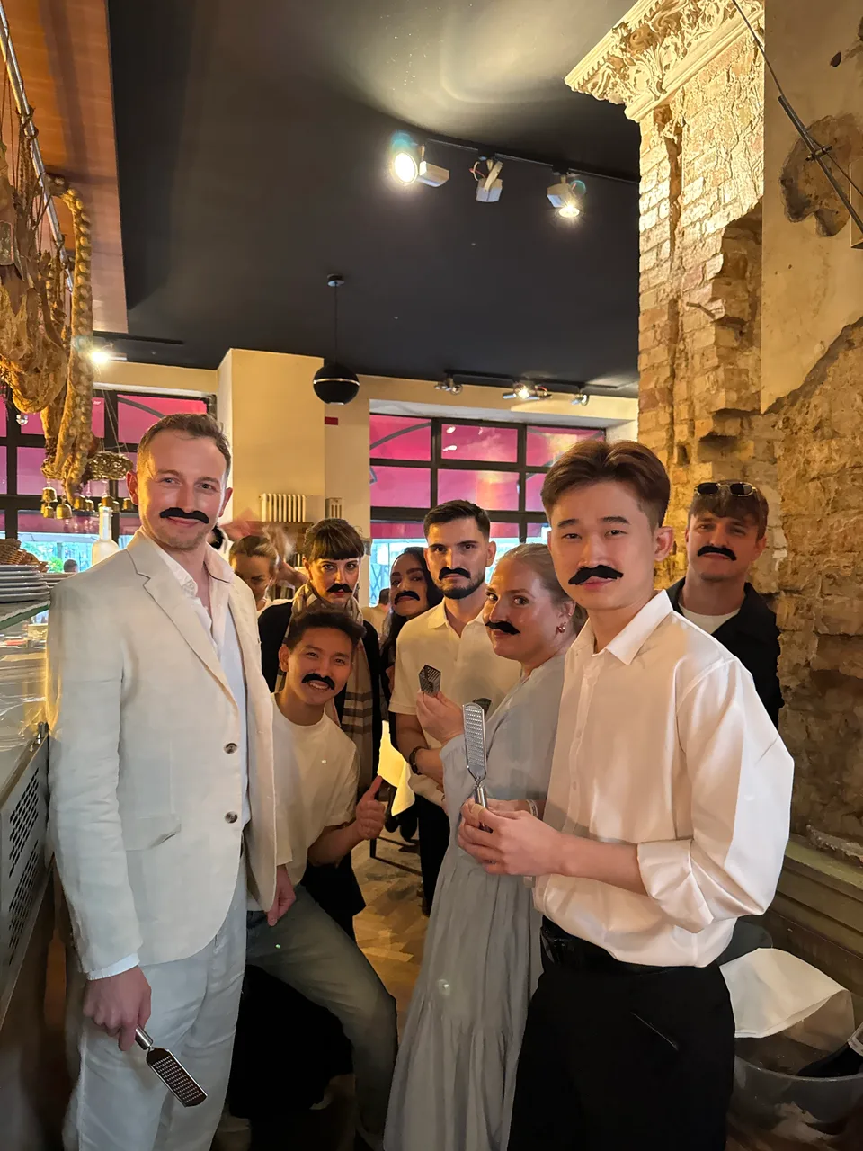 Gruppe mit aufgeklebten Schnurrbärten und Käsereiben im Restaurant