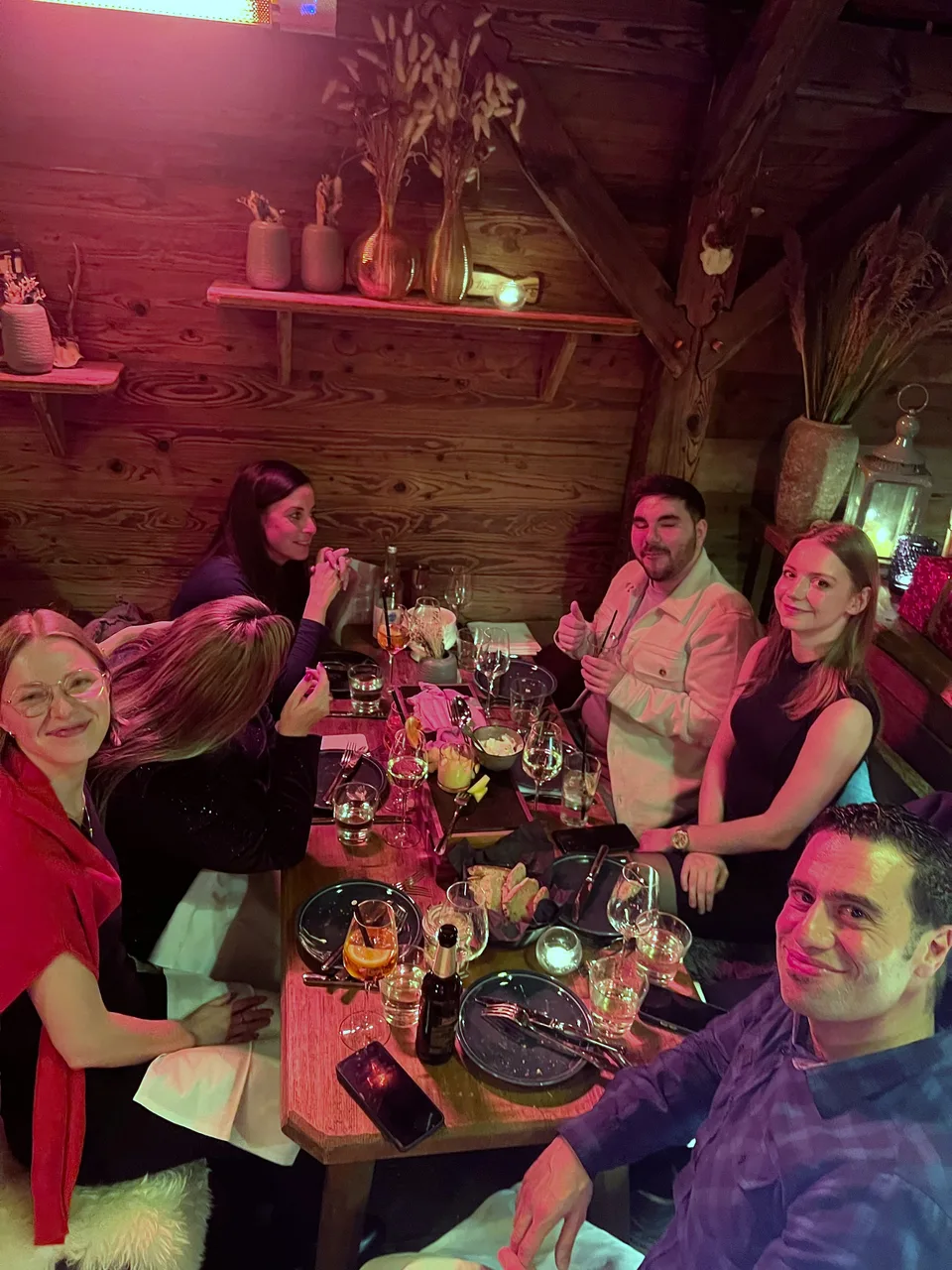 Lächelnde Tischrunde in der Holzhütte, ein Kollege zeigt Daumen hoch
