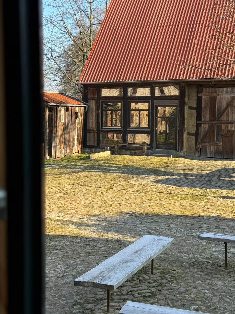 Blick durchs Fenster auf den sonnigen Hof mit Fachwerkscheune