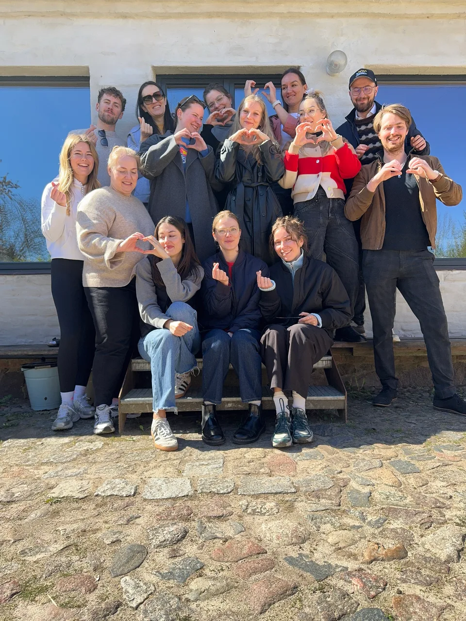 Gruppenbild mit Herz-Gesten vor dem Haus in der Sonne